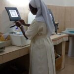 Schwester Pauline steht vor einem Optikergerät mit großen Monitor